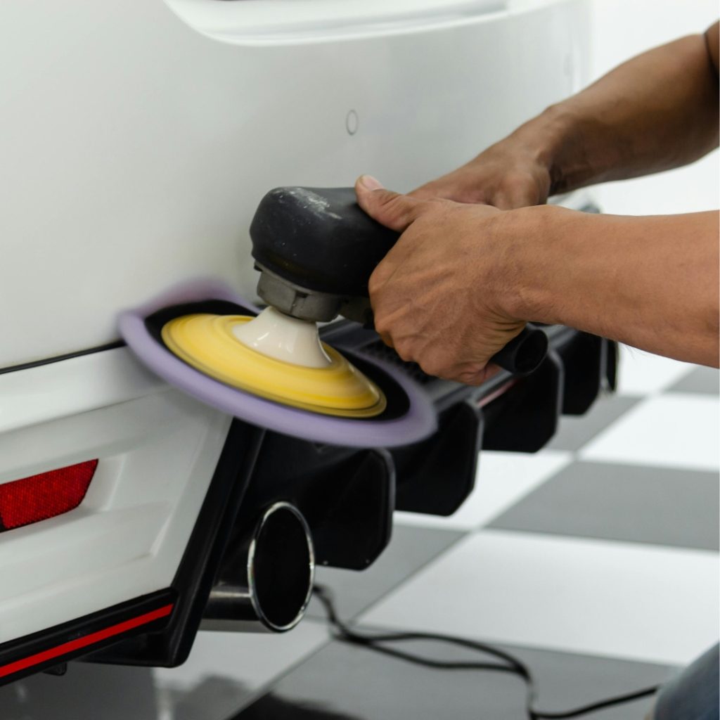 Technician using a polishing tool with yellow and white pad on white car panel during on-site repair