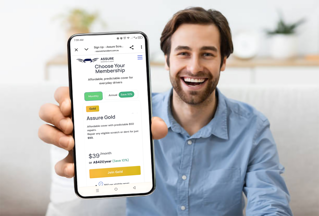 Man in blue shirt holding smartphone displaying Assure Scratch & Dent membership options including Gold plan at $39 per month
